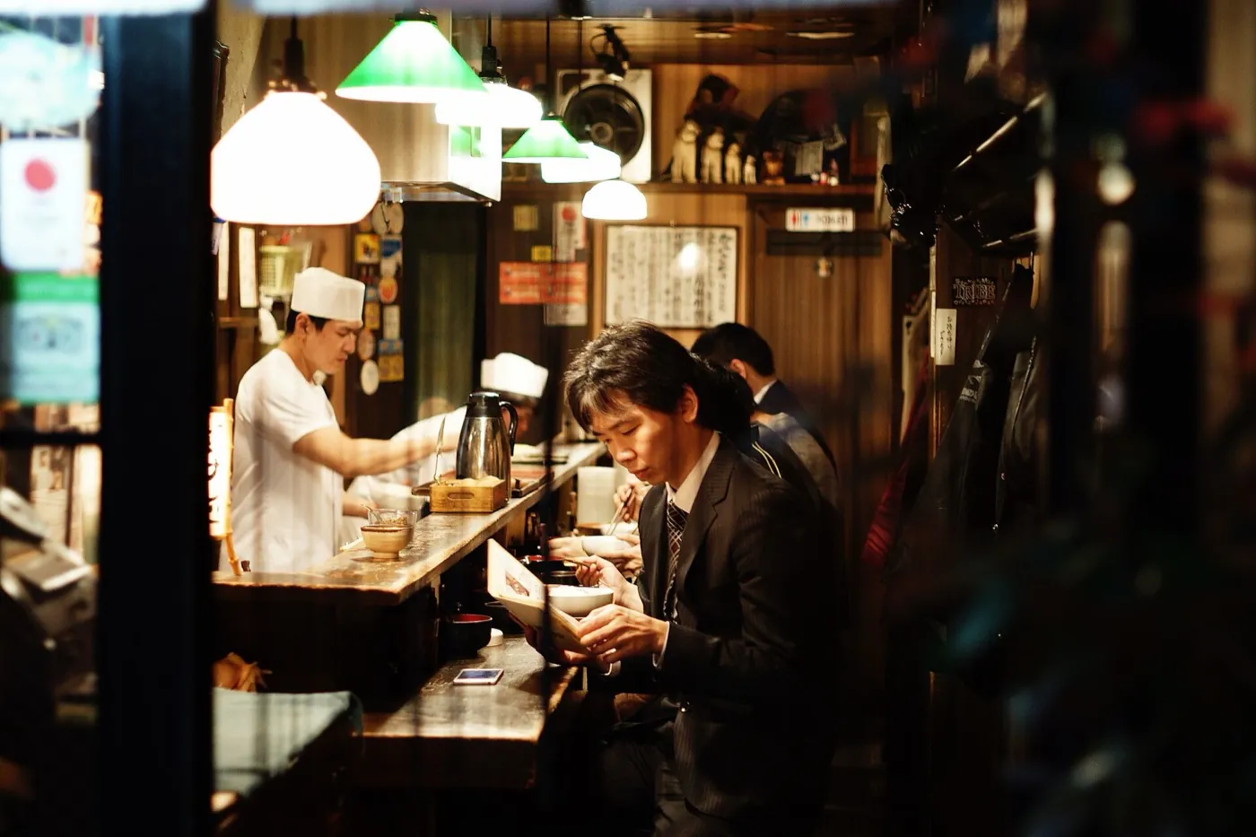 A cook serving a guest at a warm Japanese ramen counter